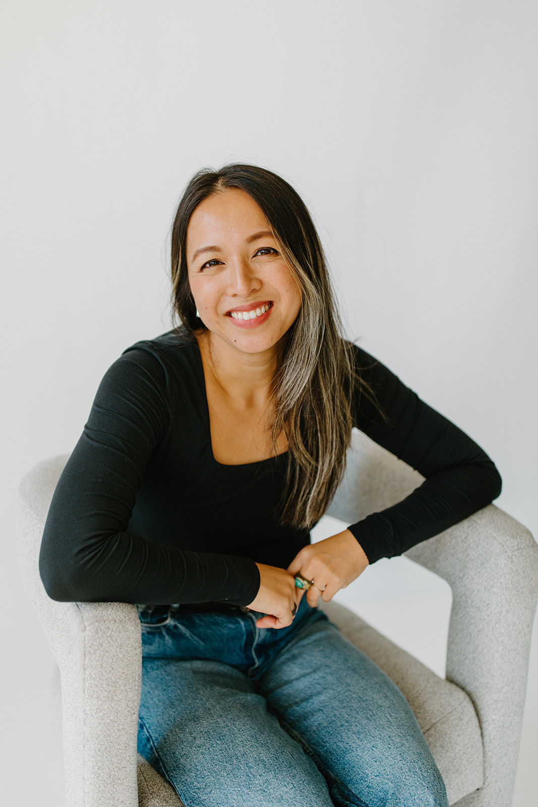 Carol Tran Reynolds smiling, seated in a gray chair
